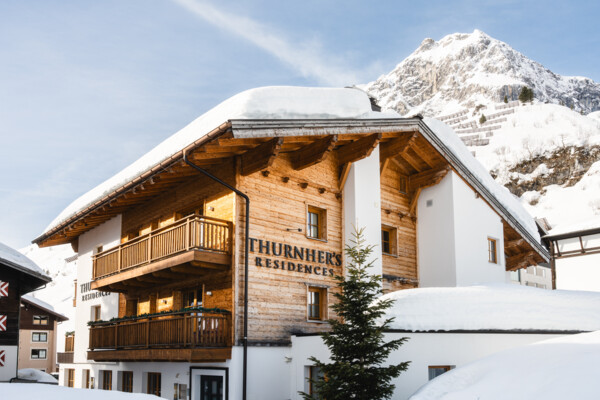Ein Haus mit der Aufschrift Thurnher’s Residences steht im Schnee und im Hintergrund ist ein schneebedeckter Berg zu sehen.