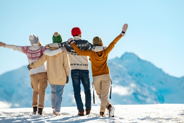 Vier Menschen stehen mit dem Rücken zur Kamera im Schnee und Blicken in die verschneite Berglandschaft.
