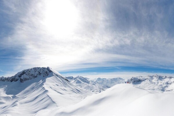 A snow-covered mountain range under a blue sky and sunshine.