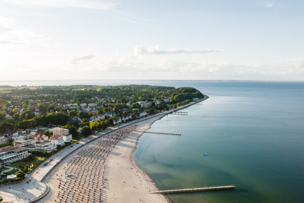 Die Ostseeküste von Travemünde von oben fotografiert mit einem breitem Strand, auf dem viele Strandkörbe stehen.